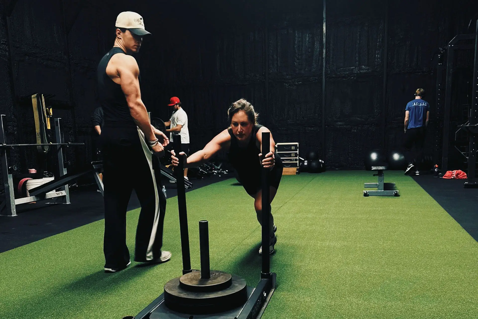 Personal training session at Mass Appeal Fitness in Winchester, TN featuring a member pushing a weighted sled on indoor turf in a 24-hour local gym.